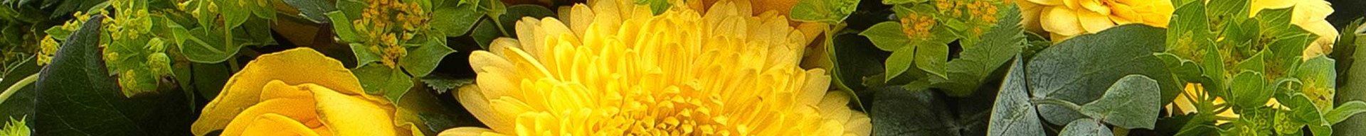 Et farverigt blomsterarrangement med gule gerberaer og roser, omkranset af grønne blade og små blomster. Den varme farvepalette skaber en livlig og glædelig atmosfære.